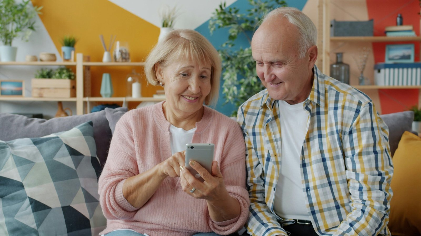 4 Best Password Managers for Elderly Parents in 2026 (Actually Easy to Use) 4 An elderly couple smiling while using a smartphone together on a couch, demonstrating a senior-friendly password manager app for easy account access.